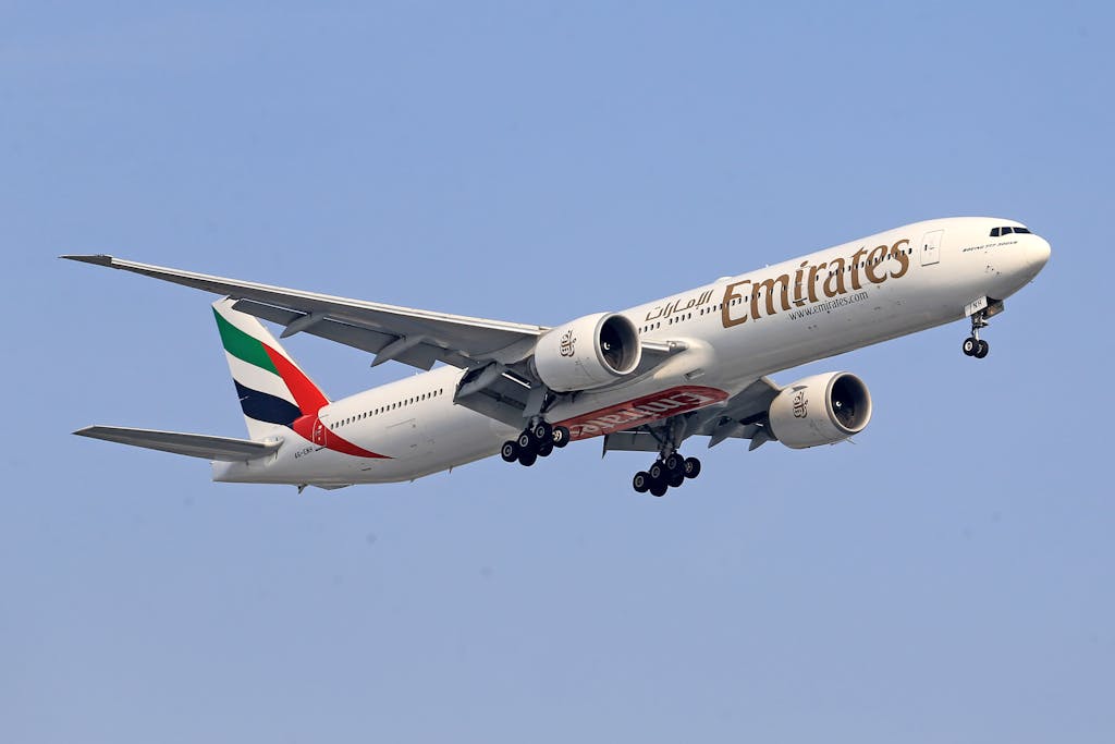 An Emirates Boeing 777 flying at cruising altitude against a clear blue sky, with its landing gear retracted.