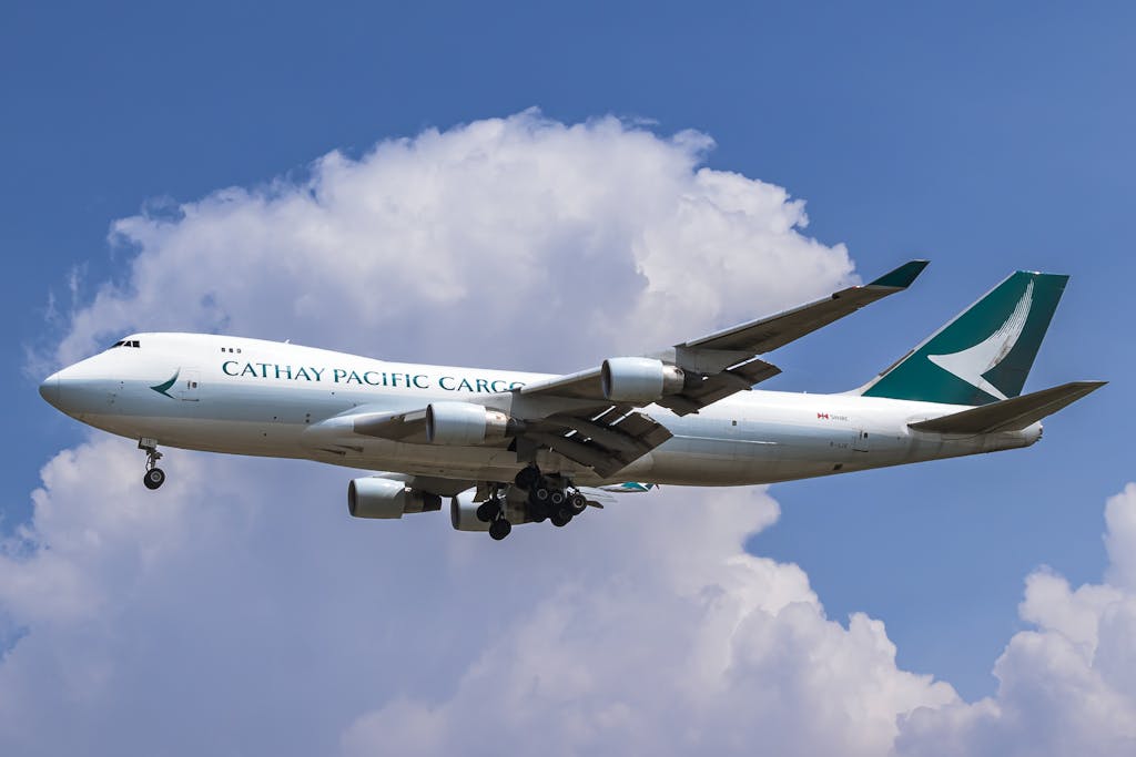 Cathay Pacific Cargo aircraft captured mid-flight against a clear blue sky with clouds in Banten, Indonesia.